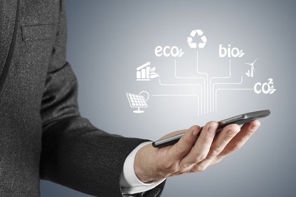 A man looking at his smartphone with icons for renewable energy sources hovering over it.