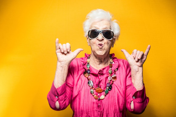 An older woman wearing a pair of sunglasses and making "hang loose" hand signs