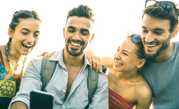 Four smiling young people looking at a smartphone