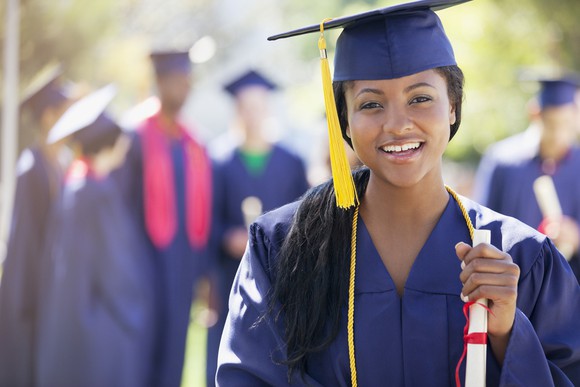 Young woman holding a rolled-up piece of paper wearing a cap and gown