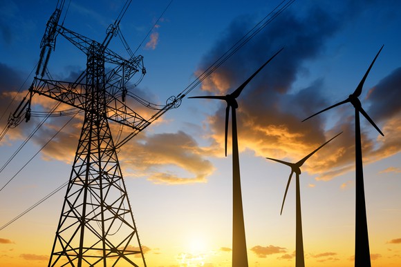 An electrical tower next to wind turbines at sunset.