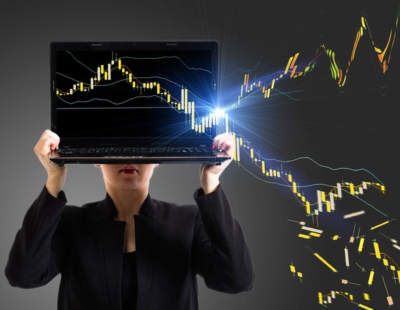 A businesswoman holding up a laptop with diverging price charts on the screen.
