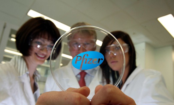 Three people in lab coats holding circular glass with Pfizer logo