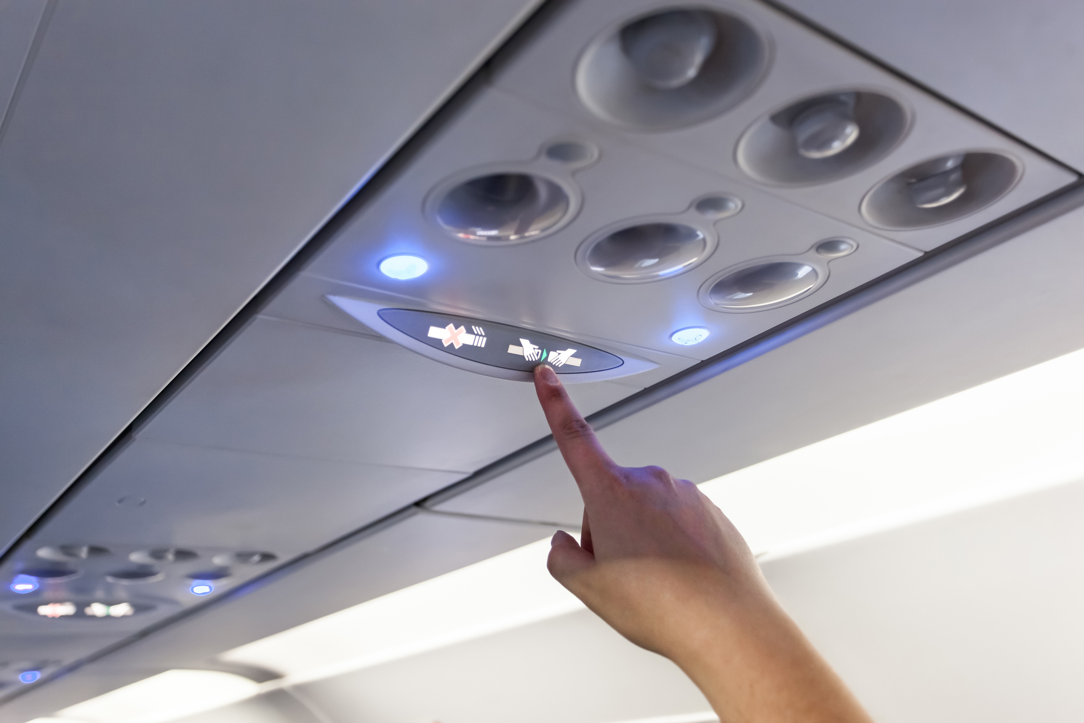 Finger pointing to "fasten seat belts" sign on airplane