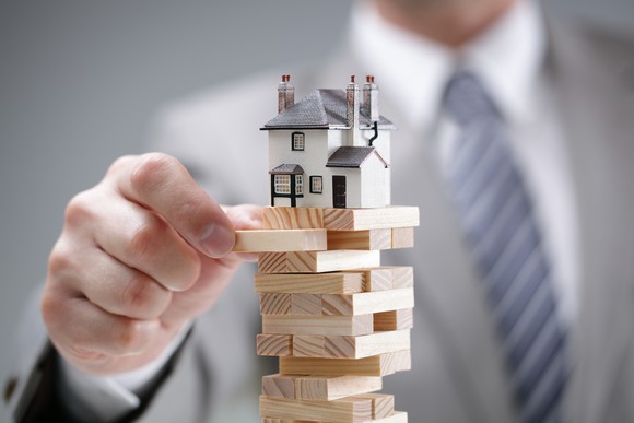 A model house placed atop a teetering stack of wooden blocks.