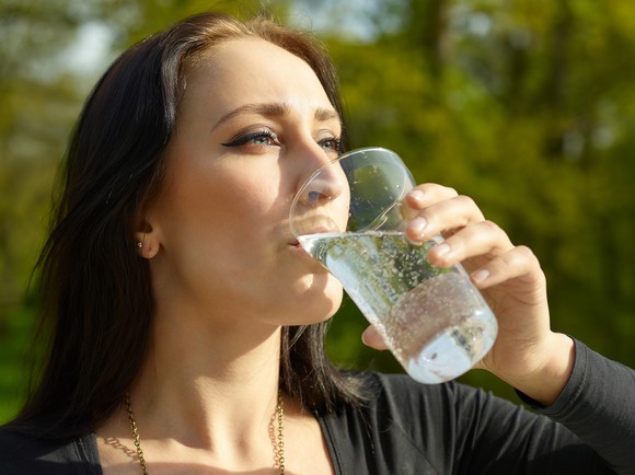 A woman drinks sparkling water.