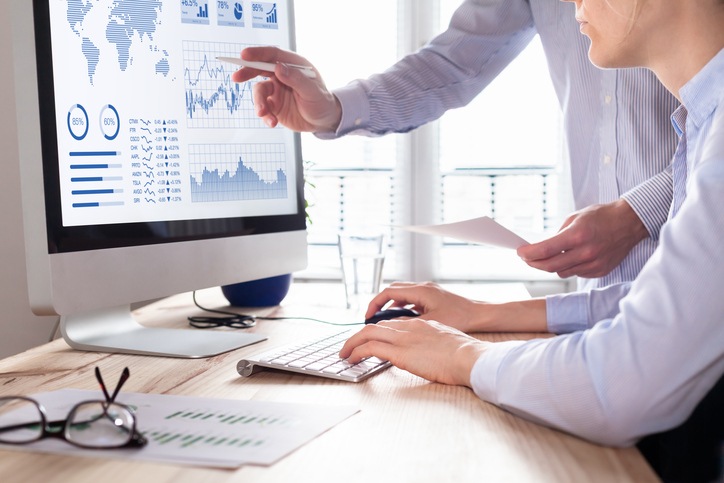 Two business people discussing an analytics dashboard displayed on a computer screen.