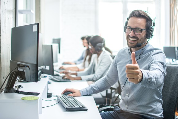 Call center representative sitting at computer, giving a thumbs-up