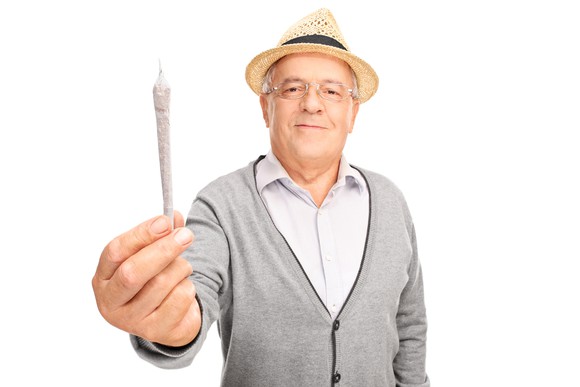 A senior man holding out a rolled cannabis joint.