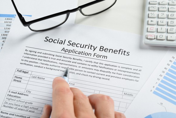 Hand holding pen, poised above a Social Security benefits application form