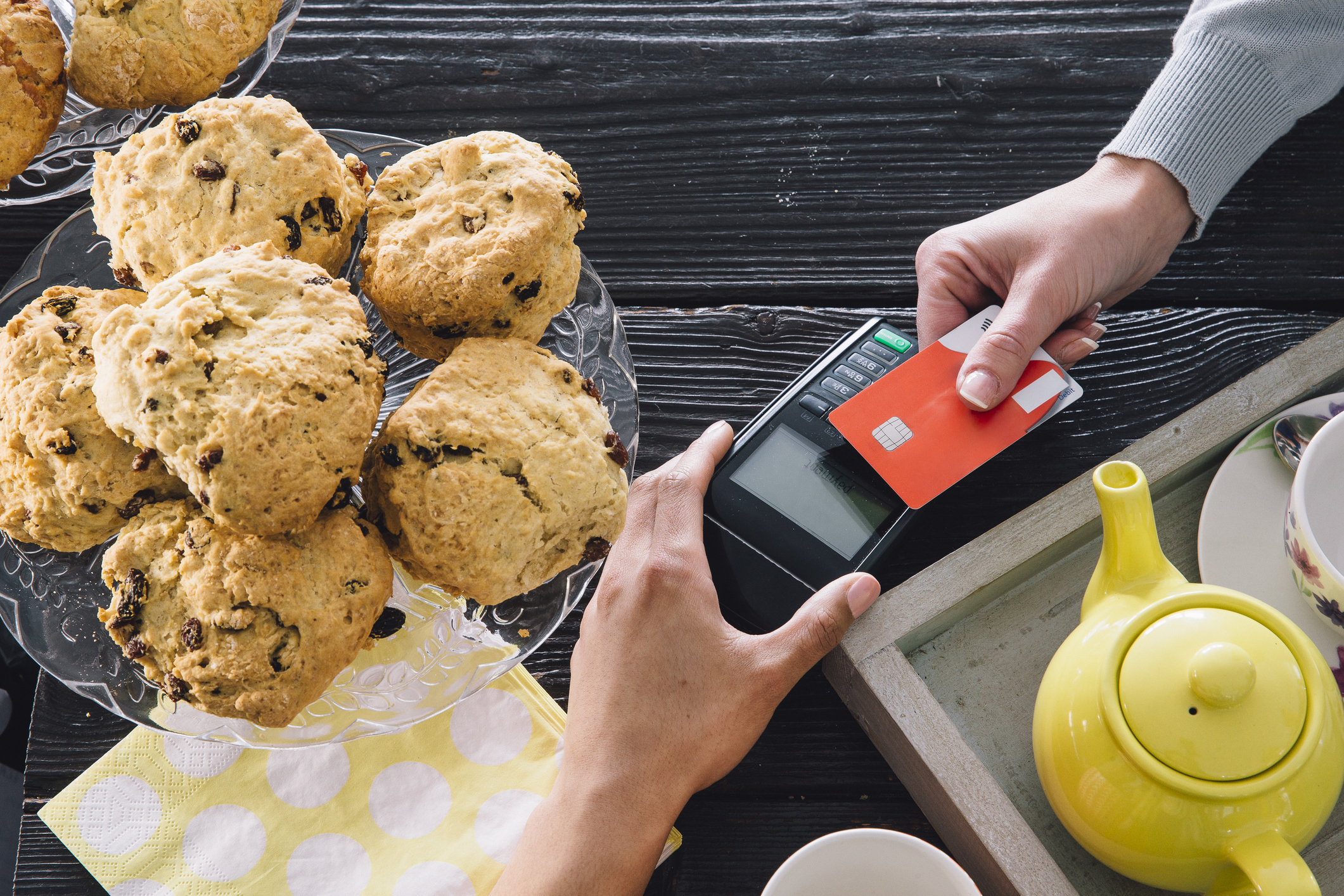Customer paying for order with contactless credit card payment over table of tea and pastries.