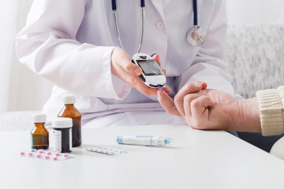 Doctor taking a patient's blood glucose level with medications on a table.