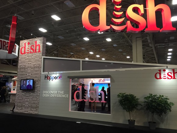 Convention hall with display for DISH, with corporate logo on the side of a mock house and window showing television display.