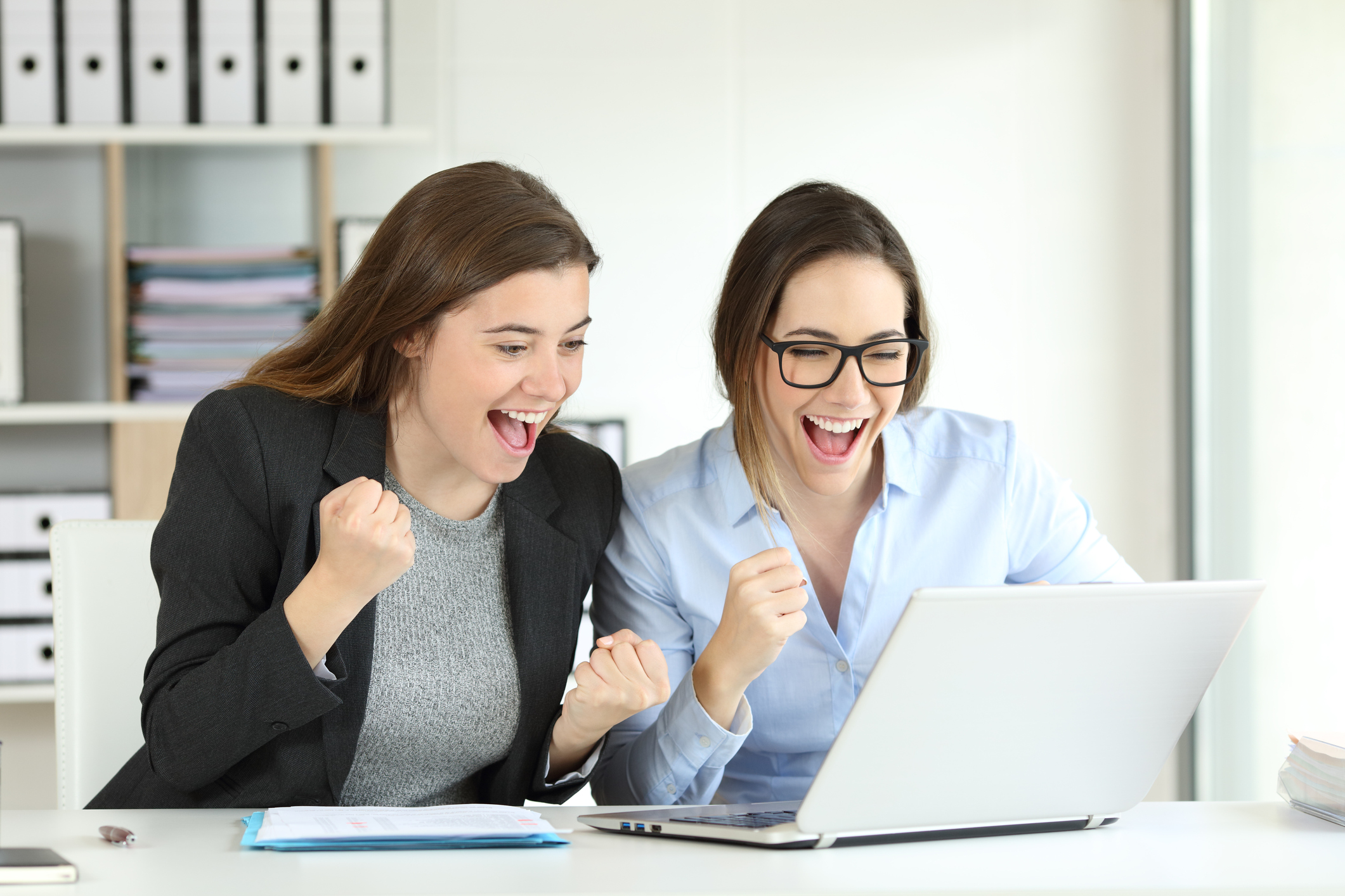 Two smiling woman pumping their right fists looking at a laptop screen