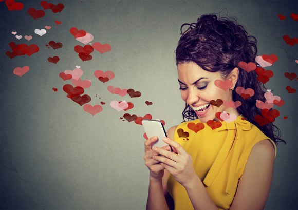 Woman smiling down at smartphone, which has cartoon hearts coming out