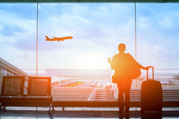 A traveler in an airport watches as an airplane takes off