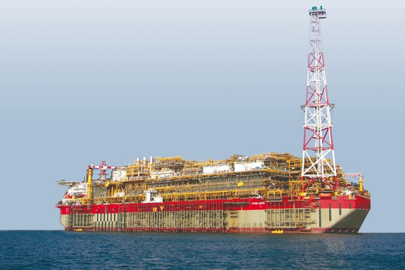 Large drillship vessel at sea with large derrick at one side of the vessel.