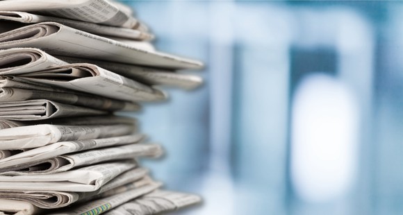 A stack of newspapers against blurred blue and white background.