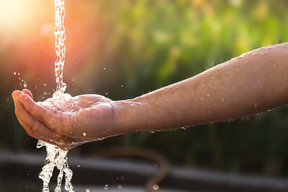 A stream of water falling from a faucet outside onto an outstretched hand.