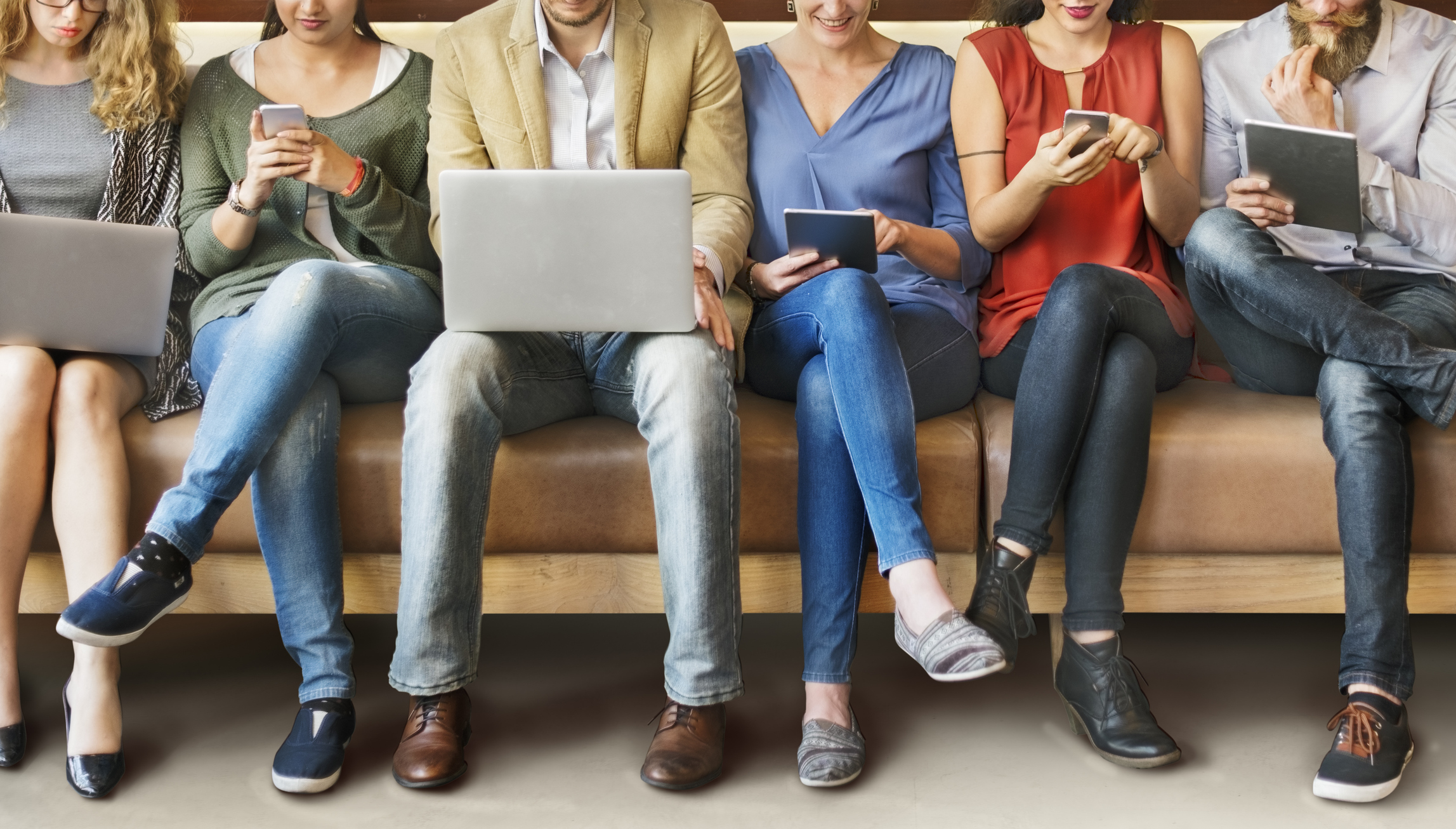 People sit on a bench using various devices.