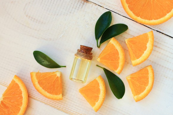 Slices of oranges scattered on a table with a small vial of citrus oil laying in the middle.