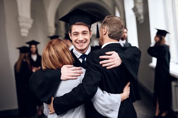 Woman and man hugging young male in cap and gown