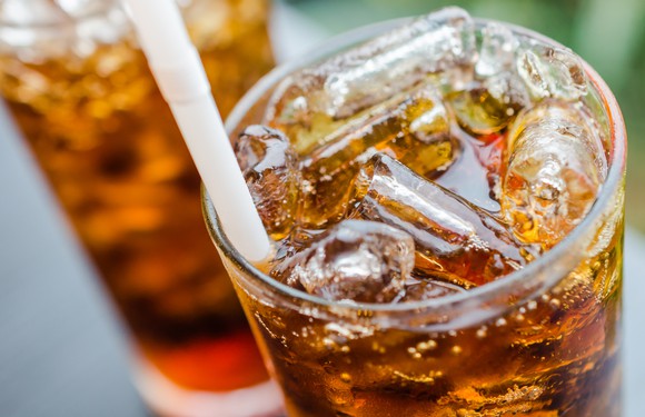 Close-up of a glass of cola with ice and a straw in it