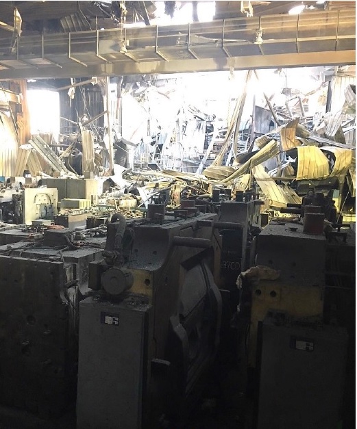 A photo of the factory floor after the fire, showing debris, tooling, and smoke damaged-walls.
