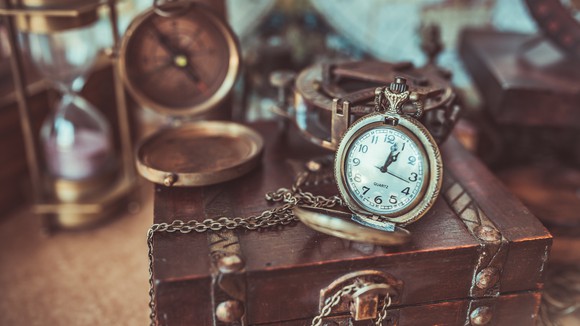 Antique box, compass, pocket watch, and hourglass on a table.