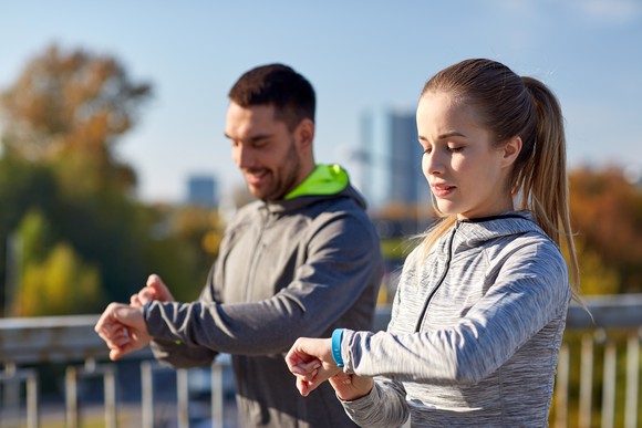 Two people check their fitness trackers.