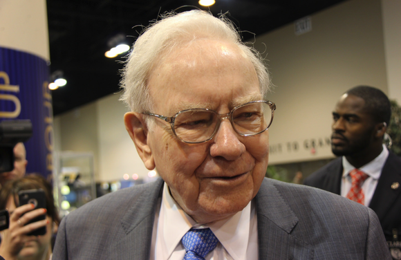 Warren Buffett smiles at someone as he walks through a crowd at a conference.