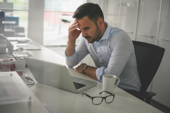 Head in hand, a troubled businessman stares at a computer screen.
