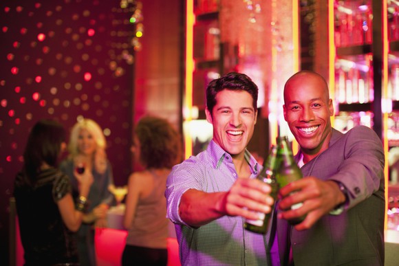 Two young men clinking bottled beers in a bar.