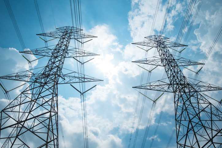 Looking up at transmission lines and towers against a cloudy blue sky.