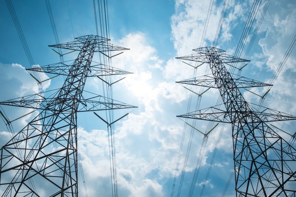 Looking up at transmission lines and towers against a cloudy blue sky.