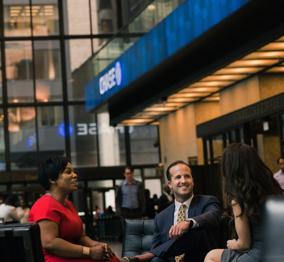 Three people in a lobby sitting in leather chairs in front of a Chase bank sign.