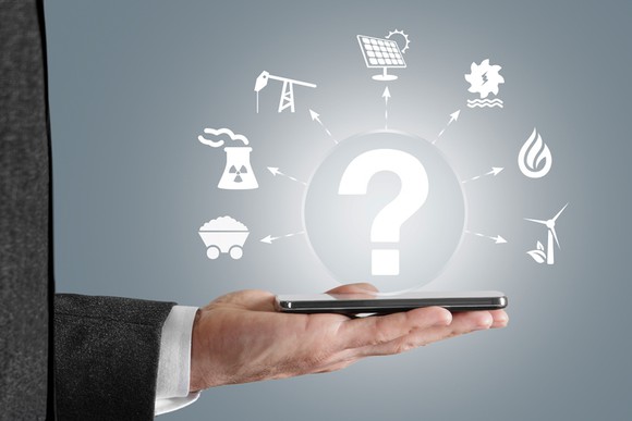A businessman holding out his smartphone flat, and it's projecting a question mark and various energy technology icons.