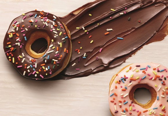 Two doughnuts with colorful sprinkles on wood table.