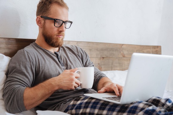 Man in pajamas working on a laptop in bed