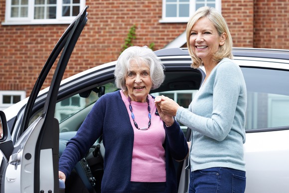 Middle-aged woman helping an older woman out of a vehicle