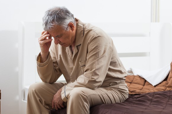 Senior man sitting in bed, holding his head