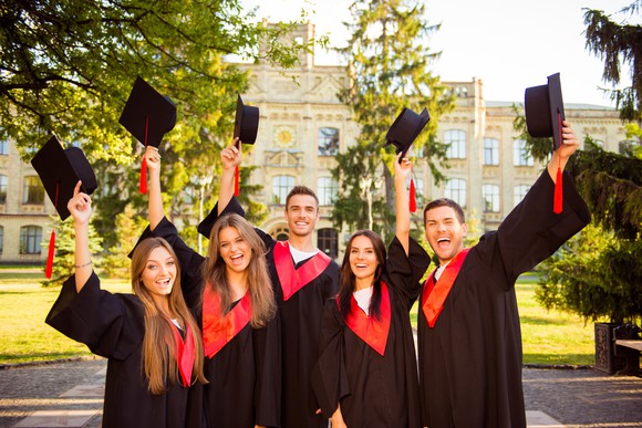 Group of young adults in graduation gowns holding up caps