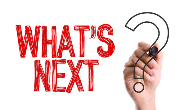 Person's hand writing "What's Next?" with a marker.
