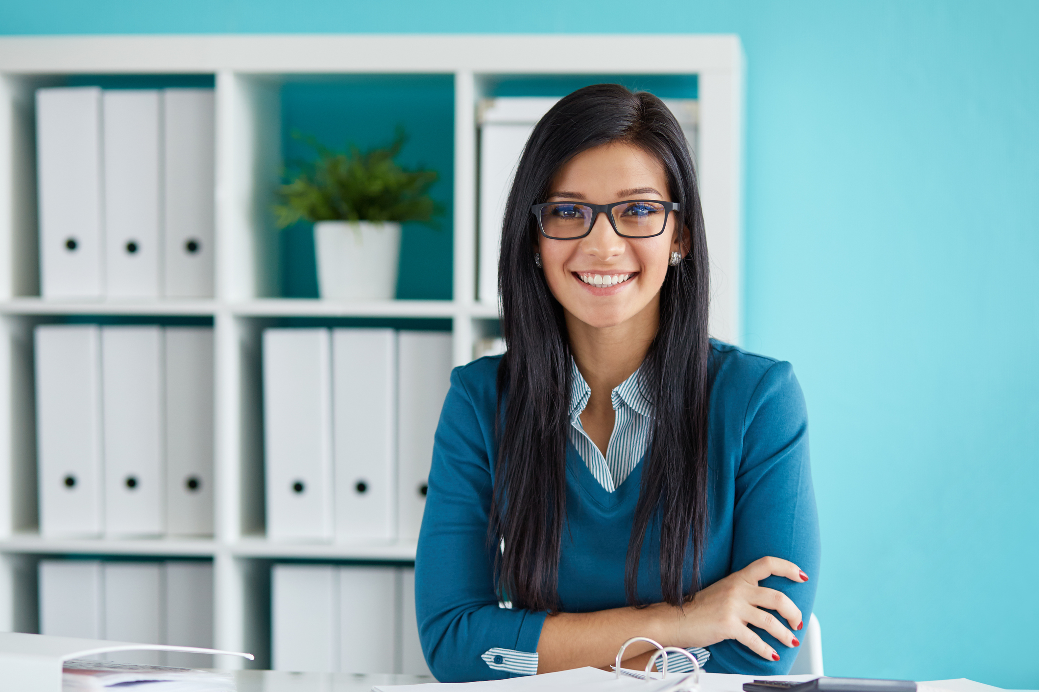 Smiling young professionally dressed woman, with her arms crossed, in front of a white cabinet