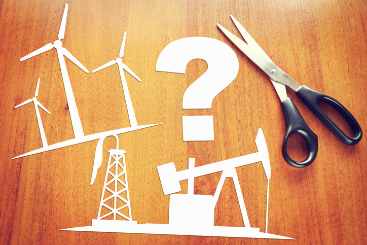 Paper cutouts of wind turbines, oil drilling, and a question mark on a desk next to a pair of scissors.