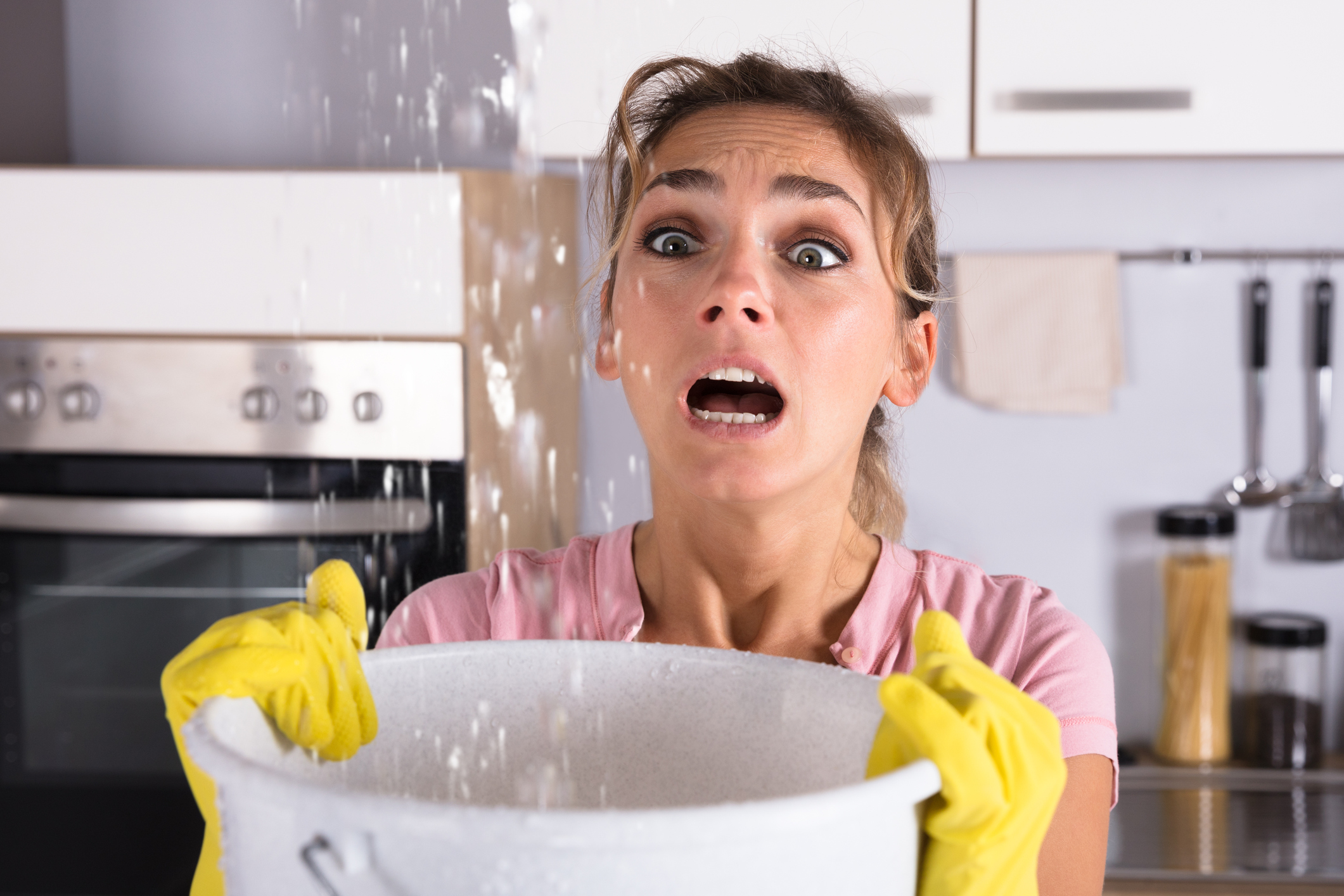 Woman holding a bucket while water pours from the ceiling