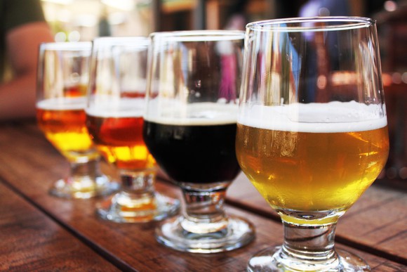 Four tulip glasses half full of different types of beer lined up on a bar