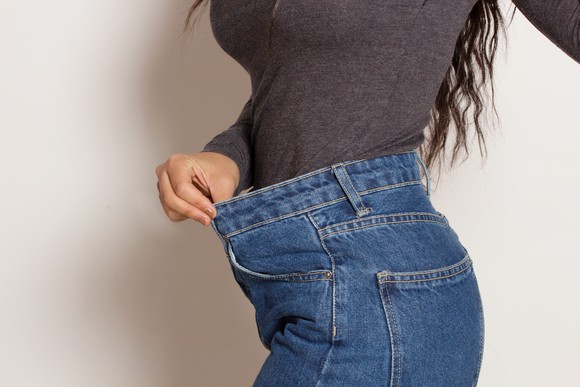 A person pulling the waistband of their jeans to show that they're too big.