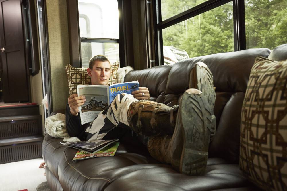 Man sitting on couch in an RV reading a magazine.