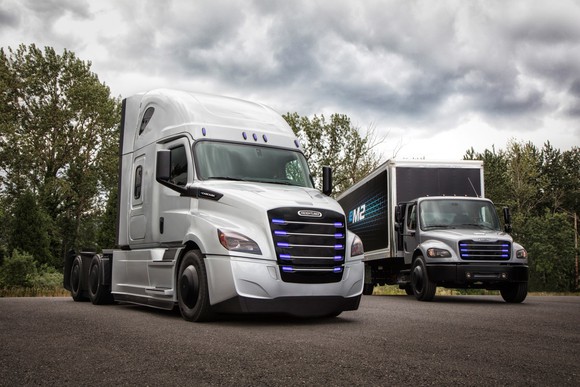 An eCascadia, a tractor-trailer truck with no trailer attached, and an eM2 106, a smallish box truck, are shown parked outside.